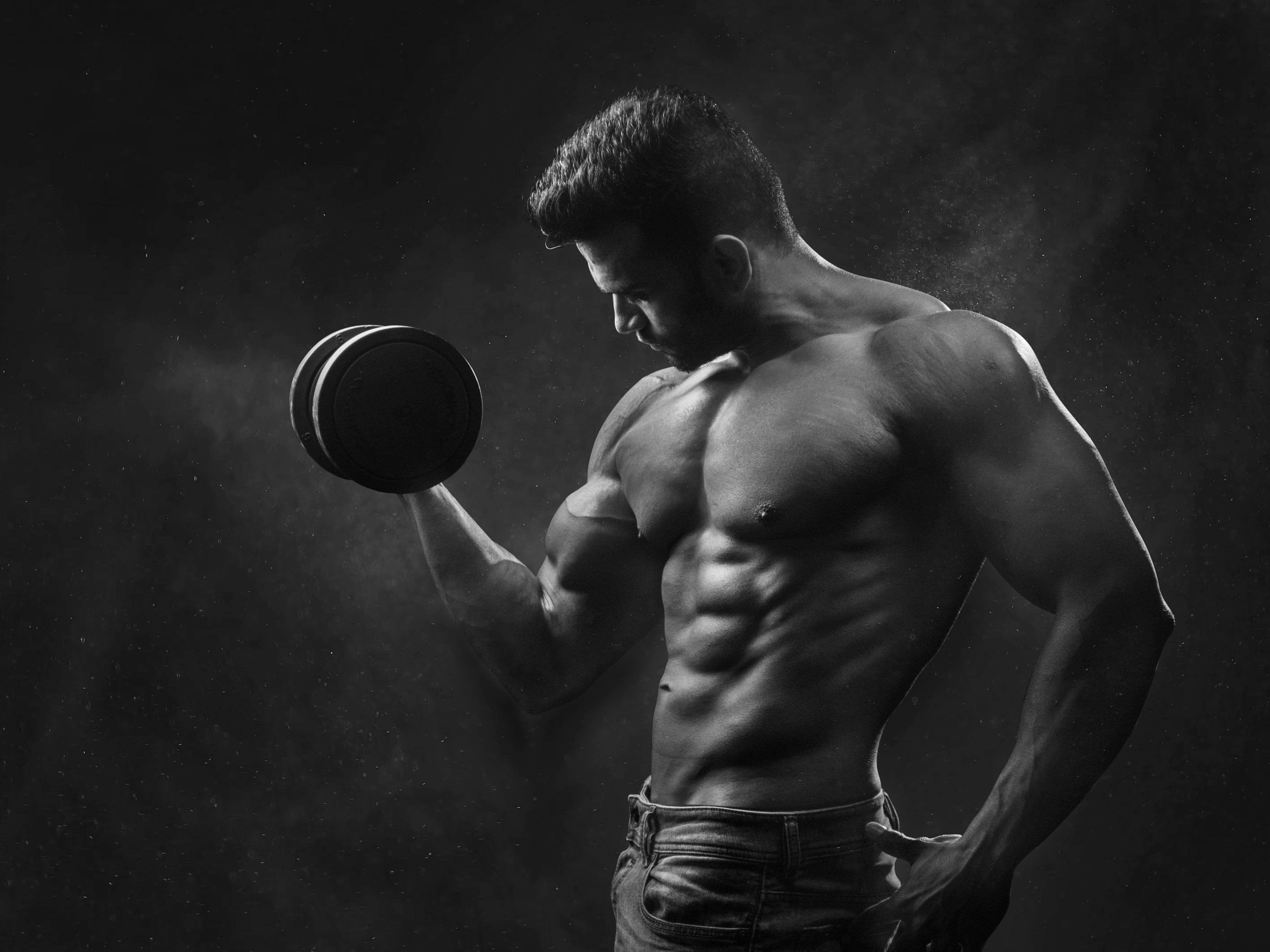 Homem musculoso malhando com haltere, treinamento, definição muscular em preto e branco.
