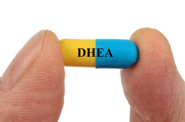 Cápsula bicolor de DHEA entre dois dedos, suplemento importado em destaque.