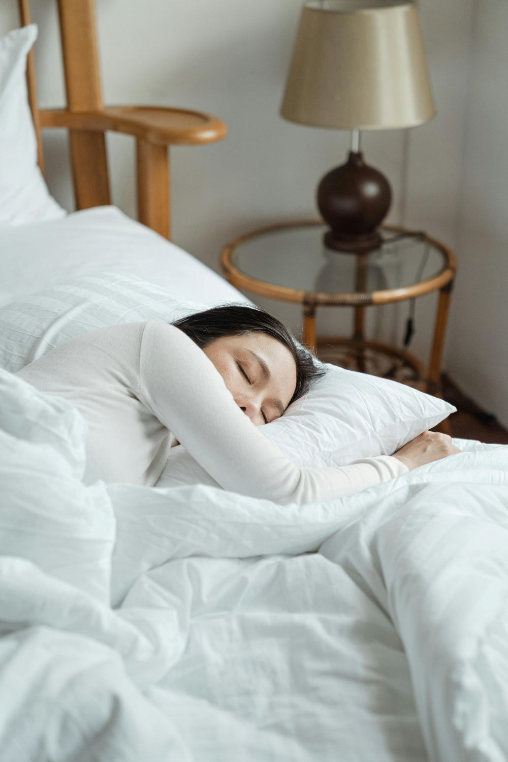 Mulher dormindo em cama branca, quarto aconchegante, sono tranquilo, descanso saudável.