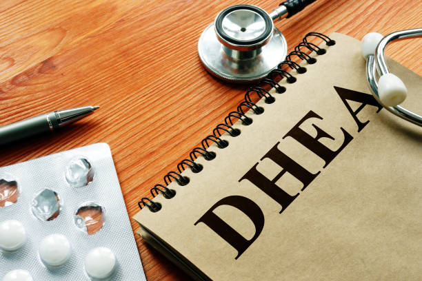 Suplemento DHEA em destaque, comprimidos, estetoscópio e bloco sobre mesa de madeira