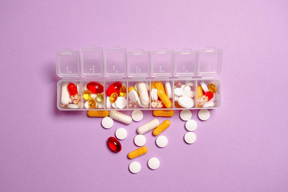 Comprimidos e cápsulas variadas em organizador de remédios sobre fundo roxo, suplementos