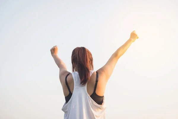 Mulher ao ar livre com braços erguidos, simbolizando saúde, energia e bem-estar