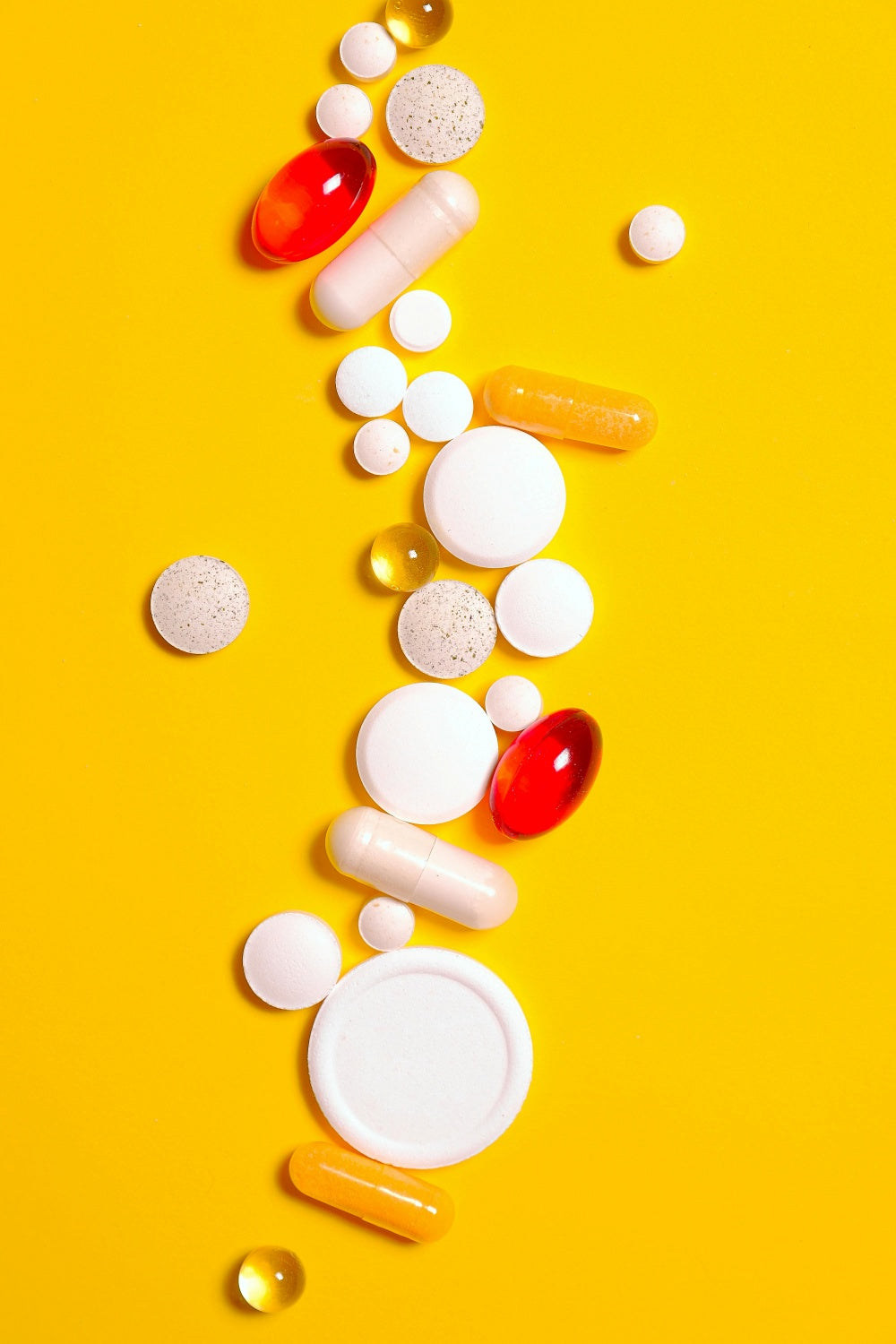 Vários suplementos, cápsulas e comprimidos coloridos sobre fundo amarelo.
