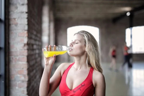 Mulher em roupa de academia bebendo suplemento esportivo amarelo após treino em ambiente interno