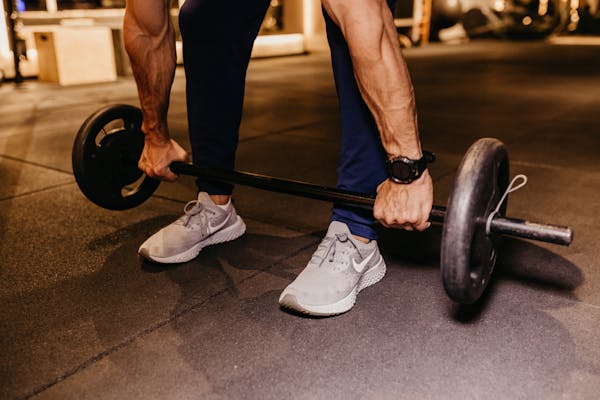 Homem em academia segurando barra de musculação, treino e fitness masculino