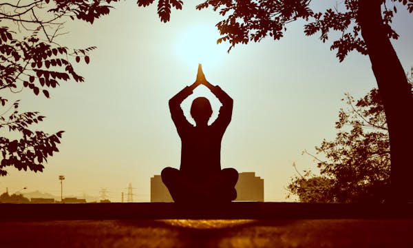 Pessoa meditando ao pôr do sol em ambiente ao ar livre, alívio do estresse e ansiedade