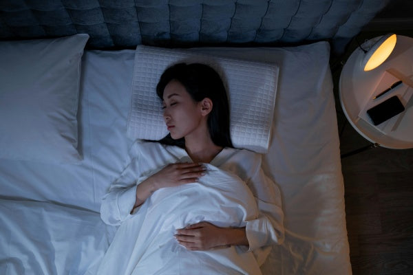 Mulher dormindo tranquilamente na cama, ambiente escuro, luz suave no criado-mudo.