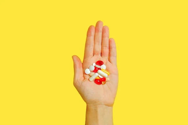 Mão segurando cápsulas e comprimidos de vitaminas importadas em fundo amarelo