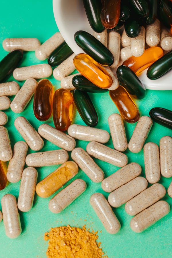 Várias cápsulas de multivitamínicos importados e suplemento em pó sobre fundo verde.