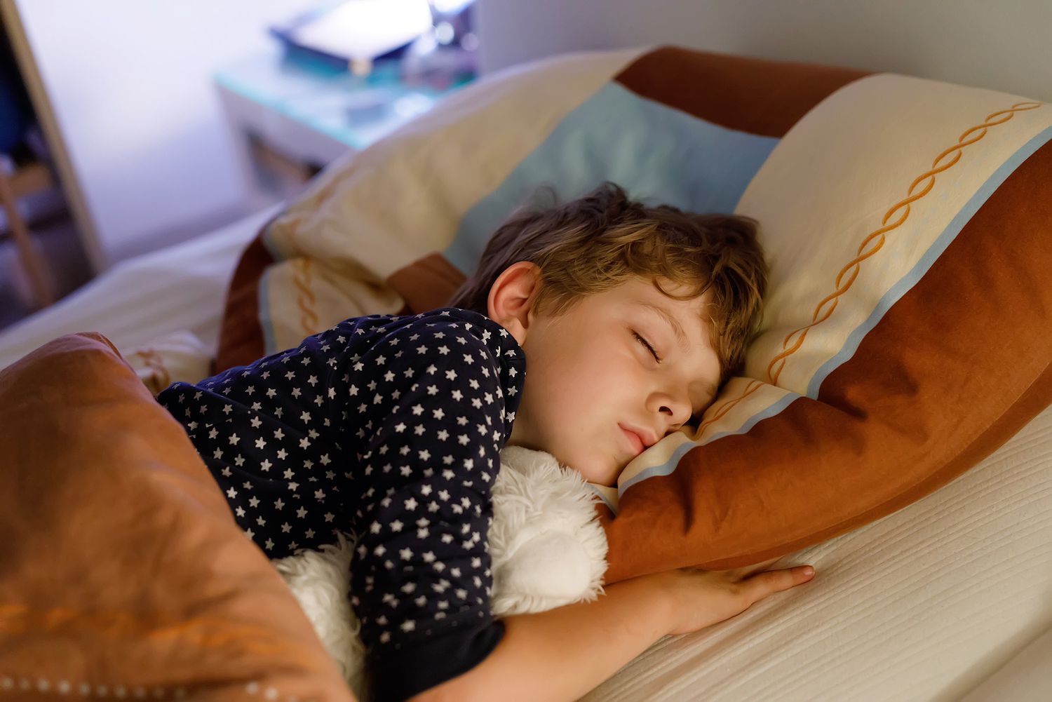 Menino dormindo tranquilamente na cama, pijama de estrelas, ambiente aconchegante, sono infantil saudável.