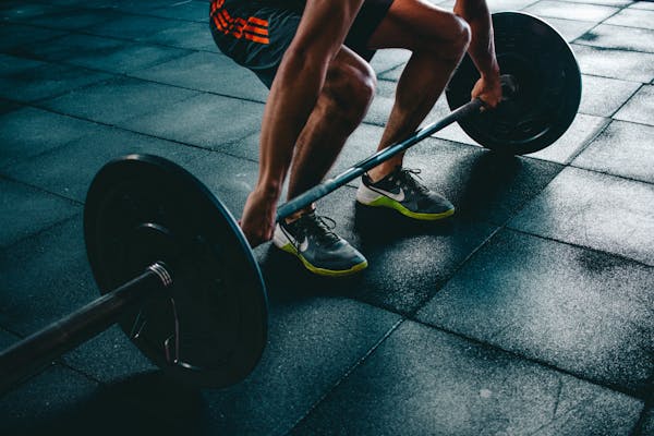 Homem levantando barra de peso em academia, treino de força para emagrecimento e definição muscular.