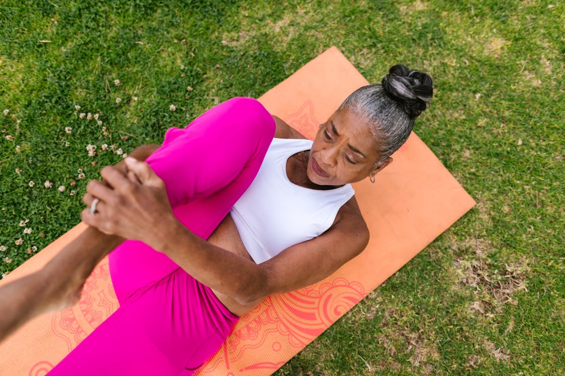 Mulher madura praticando alongamento em tapete de yoga ao ar livre, vestindo roupa esportiva.