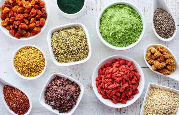 Várias tigelas com superalimentos naturais, sementes, frutas secas e pós adaptógenos coloridos.