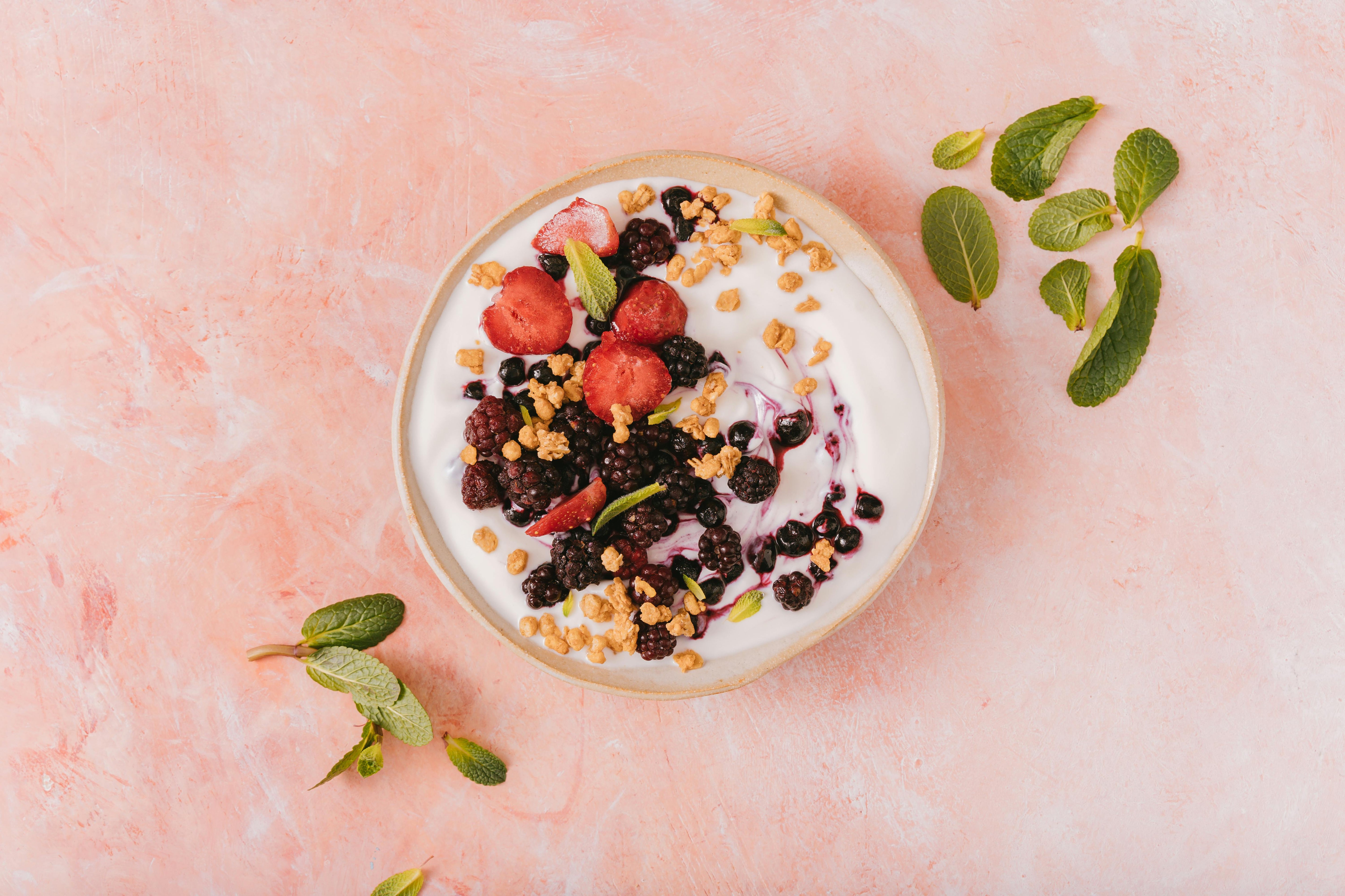 Iogurte natural com probióticos, frutas vermelhas, granola e hortelã sobre mesa rosa
