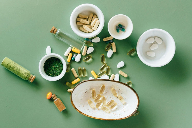 Cápsulas, comprimidos e suplementos diversos em potes sob fundo verde, variedade de suplementos alimentares.