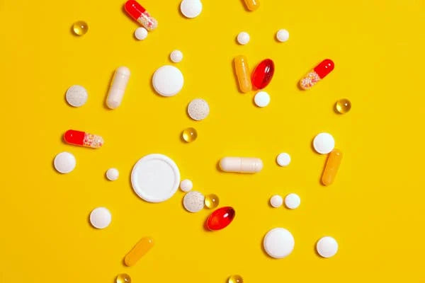 Várias cápsulas e comprimidos de suplementos alimentares sobre fundo amarelo