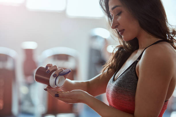 Mulher tomando suplemento pré-treino em cápsulas na academia, foco em saúde e fitness.