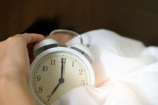 Pessoa segurando despertador clássico branco com foco em sono saudável e rotina matinal