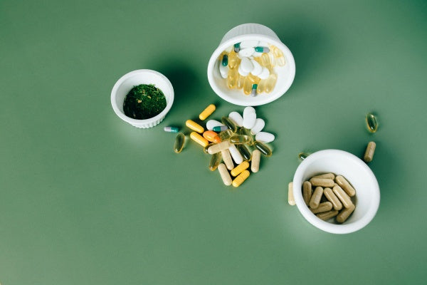 Cápsulas e comprimidos de suplementos vitamínicos em potes brancos sobre fundo verde